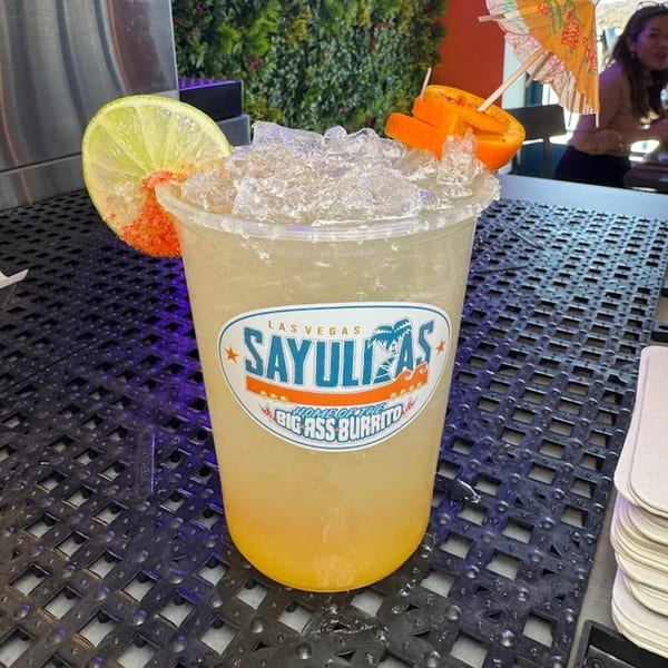 Sayulitas margarita with lime, orange, and a tiny umbrella on a dark textured table.