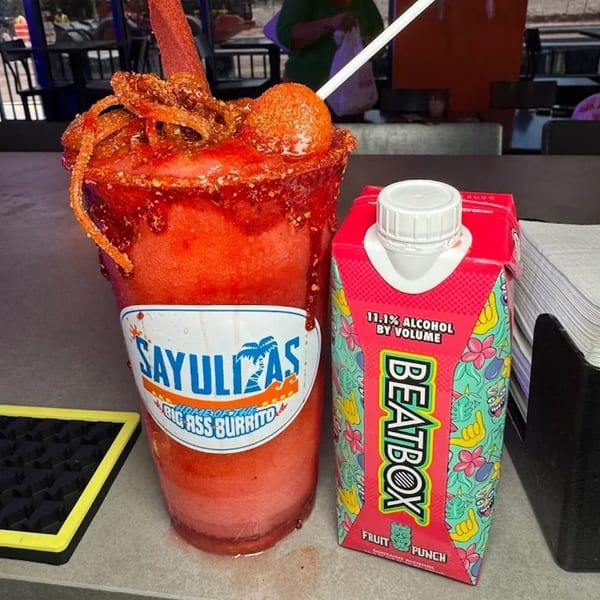 A Sayulitas branded chamoy-rimmed drink with candy and a BeatBox Fruit Punch carton on a counter.