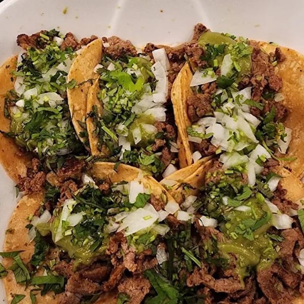 Four Sayulitas Mexican street tacos with carne asada, onions, cilantro, and green salsa.