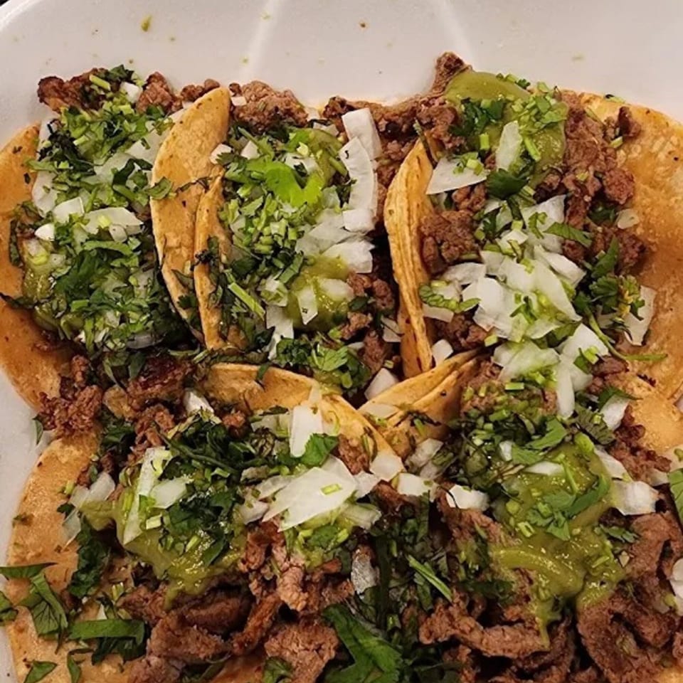 Four Sayulitas Mexican street tacos with carne asada, onions, cilantro, and green salsa.