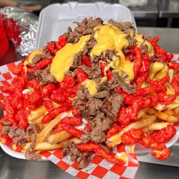 Sayulitas' carne asada fries topped with Hot Cheetos and nacho cheese in a takeout container.