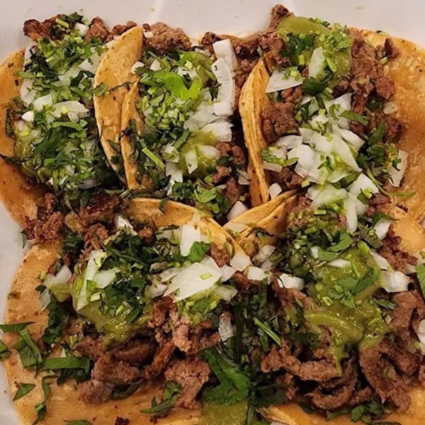 Four Sayulitas carne asada tacos with cilantro, onions, and green salsa on corn tortillas.