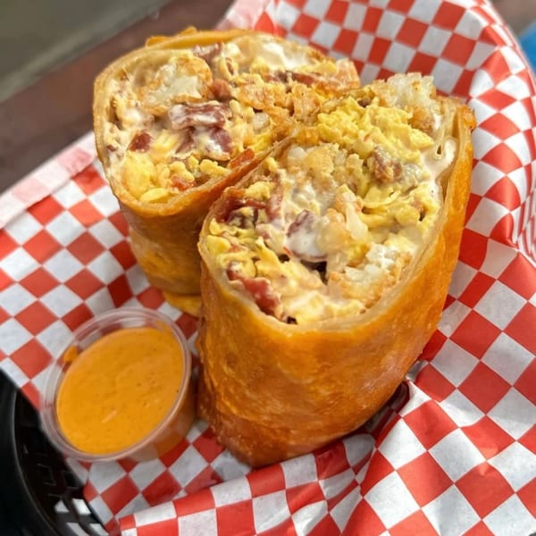 Two deep-fried burritos, cut in half, filled with scrambled eggs and bacon, served with a side of sauce.