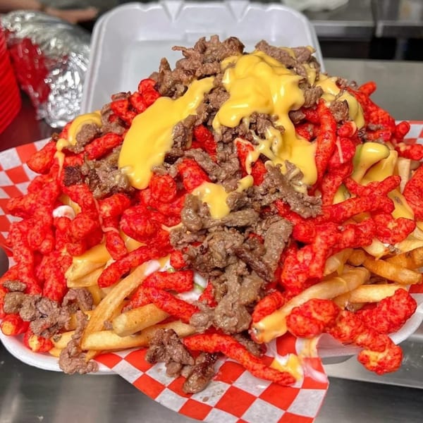 Sayulitas' loaded fries with carne asada, nacho cheese, and Hot Cheetos in a takeout container.
