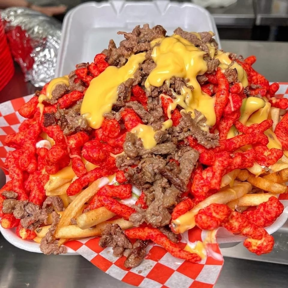 Sayulitas' loaded fries with carne asada, nacho cheese, and Hot Cheetos in a takeout container.