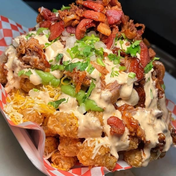 Sayulitas' loaded tater tots with various meats, cheese, sauces, and cilantro in a red checkered basket.