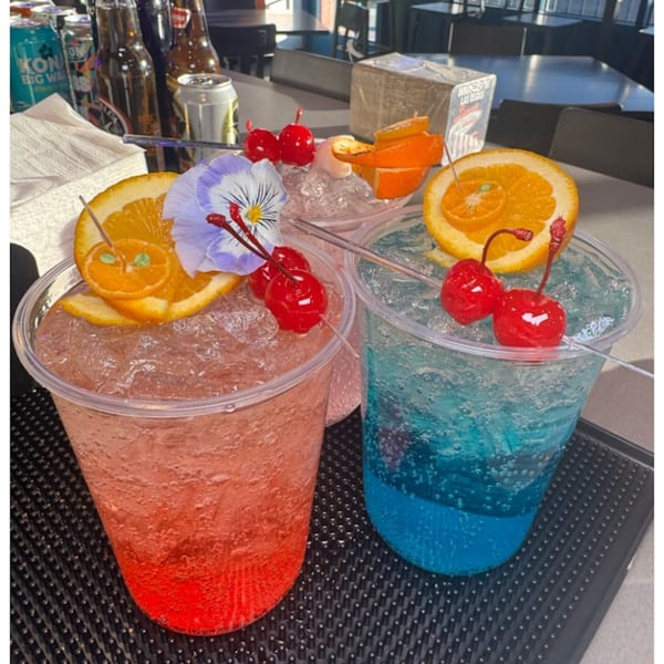 Two vibrant cocktails, one red and one blue, garnished with oranges, cherries, and a purple flower.