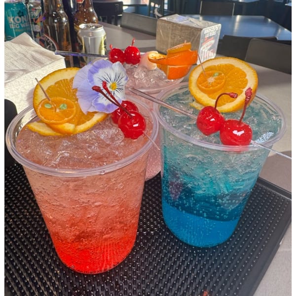 Three vibrant, fruity cocktails with orange slices, cherries, and edible flowers on a bar.