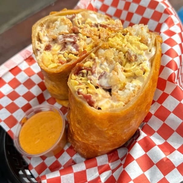 Two golden-brown, deep-fried burritos filled with scrambled eggs and bacon, served with a side of orange sauce.