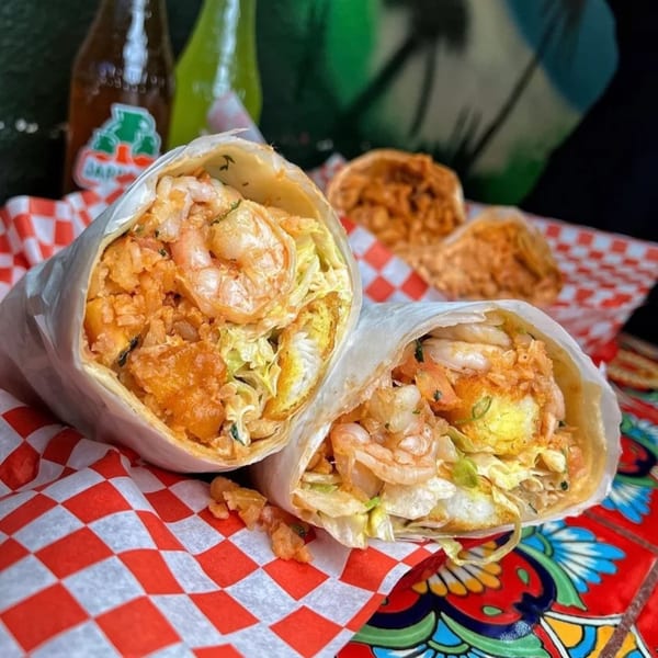 Two large shrimp burritos, wrapped in paper, on red and white checkered paper with Jarritos bottles.
