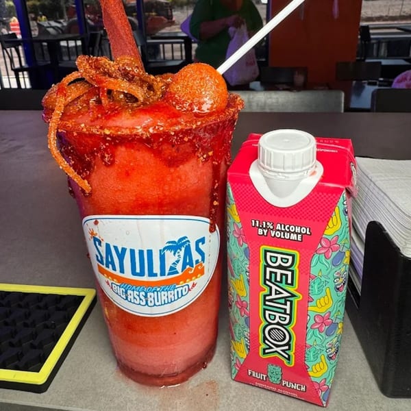 A Sayulitas branded red frozen drink with candy and a BeatBox Fruit Punch carton on a counter.