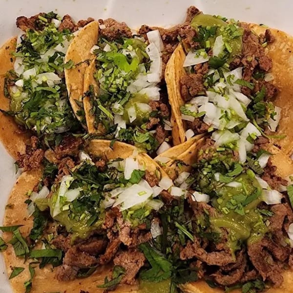 Four Sayulitas Mexican street tacos with carne asada, onions, cilantro, and green salsa.