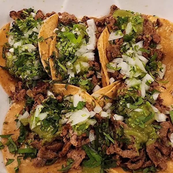 Close-up of four Sayulitas Mexican street tacos with carne asada, onions, cilantro, and green salsa.
