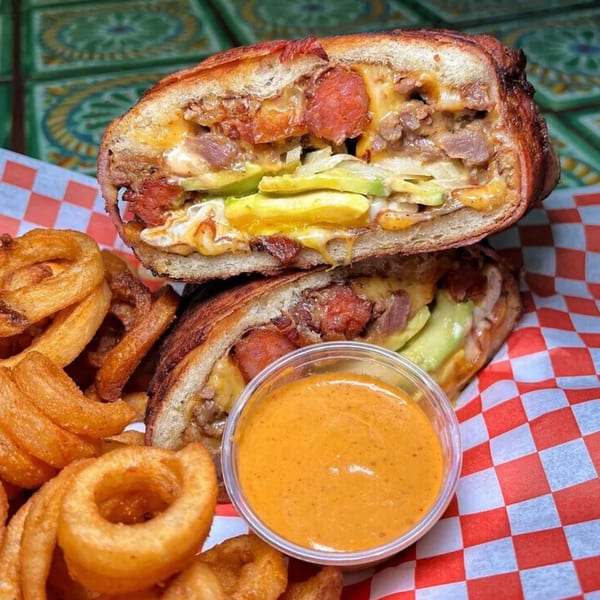 A Sayulitas Mexican torta sandwich, cut in half, with curly fries and dipping sauce.