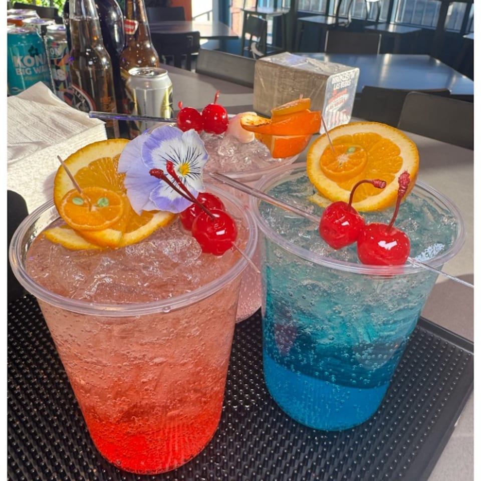 Three vibrant Sayulitas cocktails, garnished with oranges, cherries, and a purple flower, on a bar.
