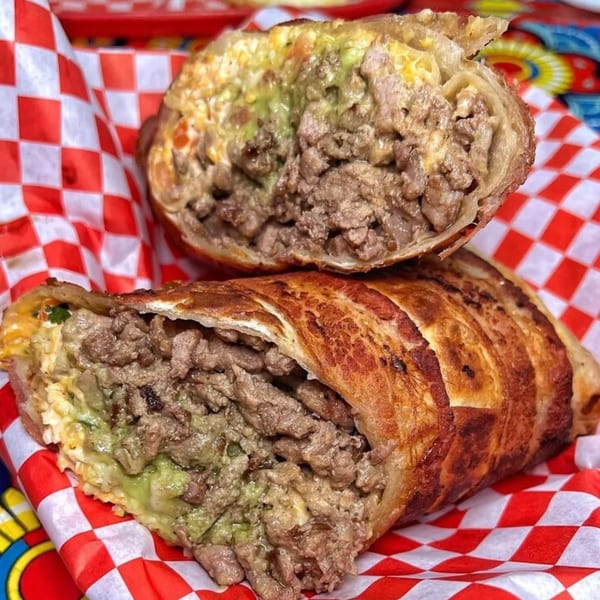 Two halves of a crispy, golden-brown Mexican burrito, revealing a hearty filling of meat and guacamole.