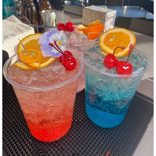 Three vibrant, fruity drinks with cherries and orange slices, one garnished with a purple flower.