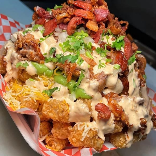 Sayulitas' loaded tater tots with various meats, sauces, cheese, and cilantro in a red and white checkered basket.