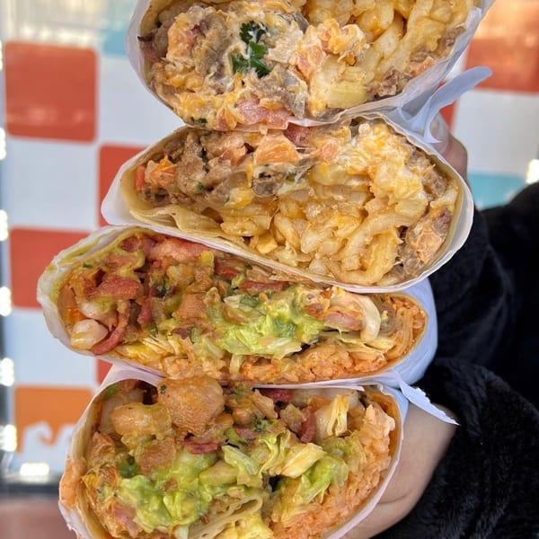 Four large, open Sayulitas burritos stacked, revealing fillings like meat, fries, rice, and guacamole.