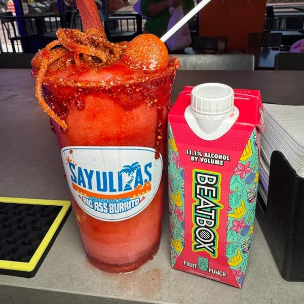 A Sayulitas branded chamoy-rimmed drink with candy, next to a Beatbox Fruit Punch carton.