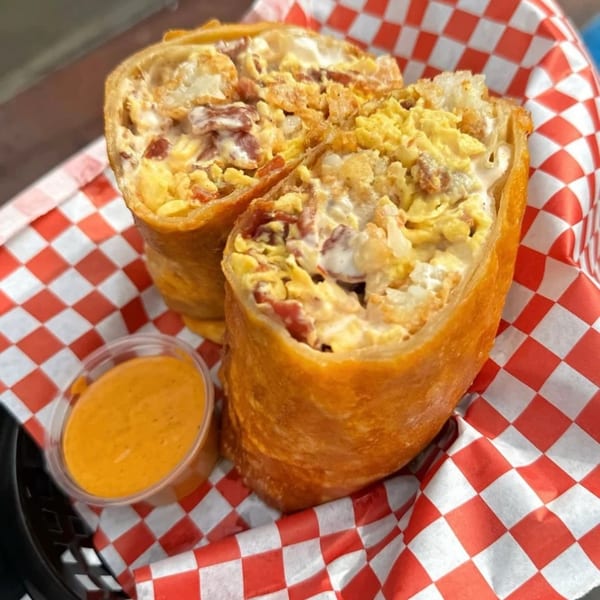 Two halves of a crispy, golden-brown breakfast burrito filled with eggs, bacon, and cheese.