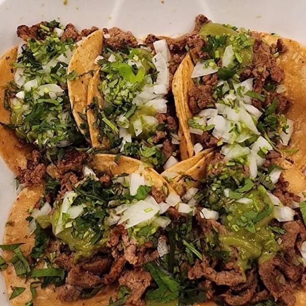 Close-up of several Sayulitas carne asada tacos with cilantro, onions, and green salsa.