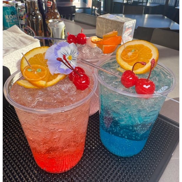 Two vibrant Sayulitas drinks, one red and one blue, garnished with oranges, cherries, and a flower.