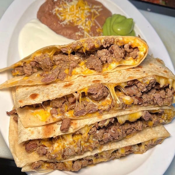 Sayulitas' carne asada quesadillas with melted cheese, served with refried beans, sour cream, and guacamole.