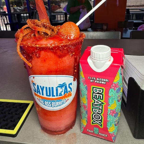A Sayulitas chamoy-rimmed drink with a Beatbox Fruit Punch carton on a counter.